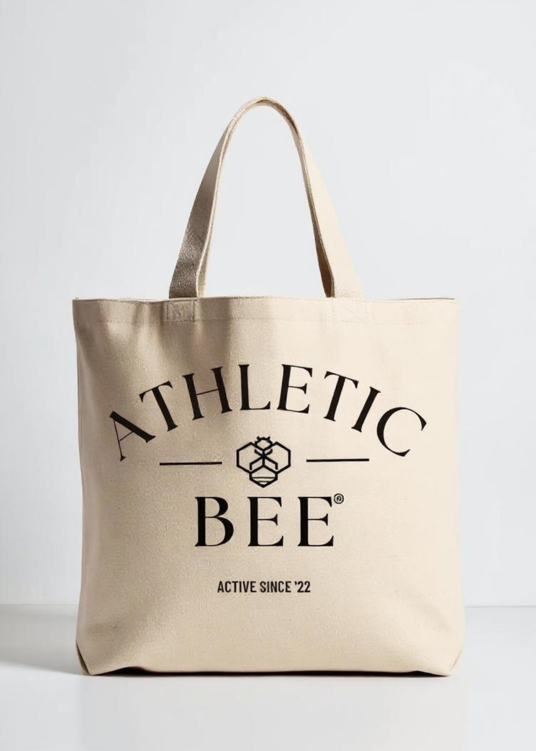 Beige tote bag with 'Athletic Bee' branding on a light gray background